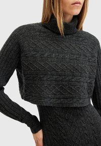 Sötétszürke cropped pulóver texturált kábel kötött mintával, magas nyakkal és bordázott ujjal. Sim gyors szál, testhezálló fazon.