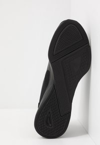 Suola nera di sneaker con gomma testurizzata, profilo a motivi e un logo a forma di diamante, inclinata su uno sfondo bianco.