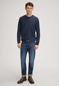 Felpa a righe blu navy con maniche lunghe, abbinata a jeans blu e stivali alla caviglia marroni. La maglietta presenta un design testurizzato e polsini a costine.