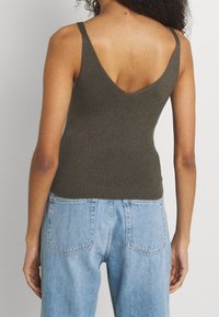 Oliwkowy prążkowany top na ramiączkach z niskim dekoltem w kształcie litery V, dopasowany krój i szerokie ramiączka, w połączeniu z jasnoniebieskimi spodniami dżinsowymi o wysokim stanie.