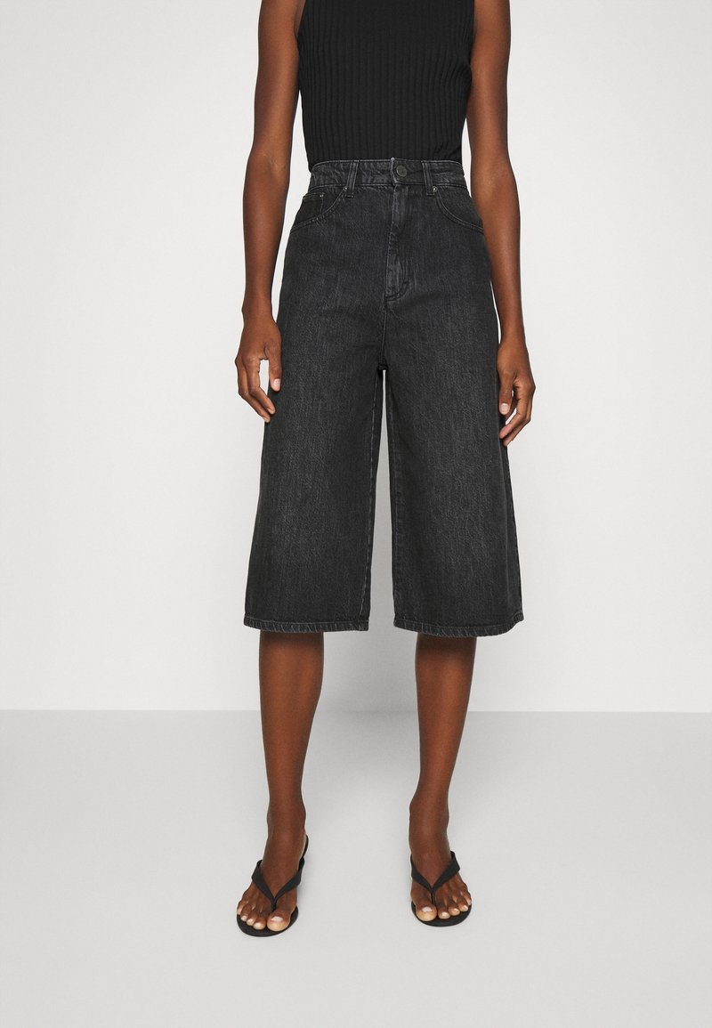 Mustat denimin culottes-housut, joissa on korkeavyötärö, leveät lahkeet ja raaka helma. Yhdistetty mustaan ribbineulottuun hihattomaan toppiin ja mustiin varvassandaaleihin.