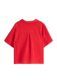Top corto a maniche corte di colore rosso con texture, dotato di colletto e caratterizzato da un dettaglio plissettato sulla schiena, realizzato in un tessuto leggero e traspirante.