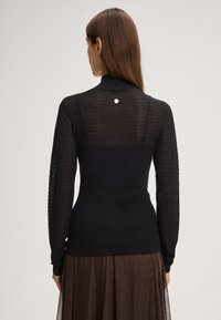 Maglione nero a maglia con un motivo testurizzato, maniche lunghe e una silhouette aderente. Presenta un piccolo accento argento sul retro.