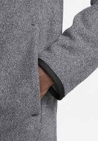 Gray wool coat featuring a textured finish, black trim on the cuff, and a side pocket positioned near a person’s hand.