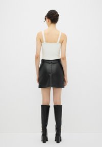 Zwarte neplederen minirok met een ritssluiting, gecombineerd met een witte tanktop en zwarte kniehoge laarzen met hak.