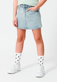 Falda mini de denim en azul claro con una cintura ajustada, cinco bolsillos y un lavado sutil. Combinada con zapatillas blancas y calcetines con rayos.