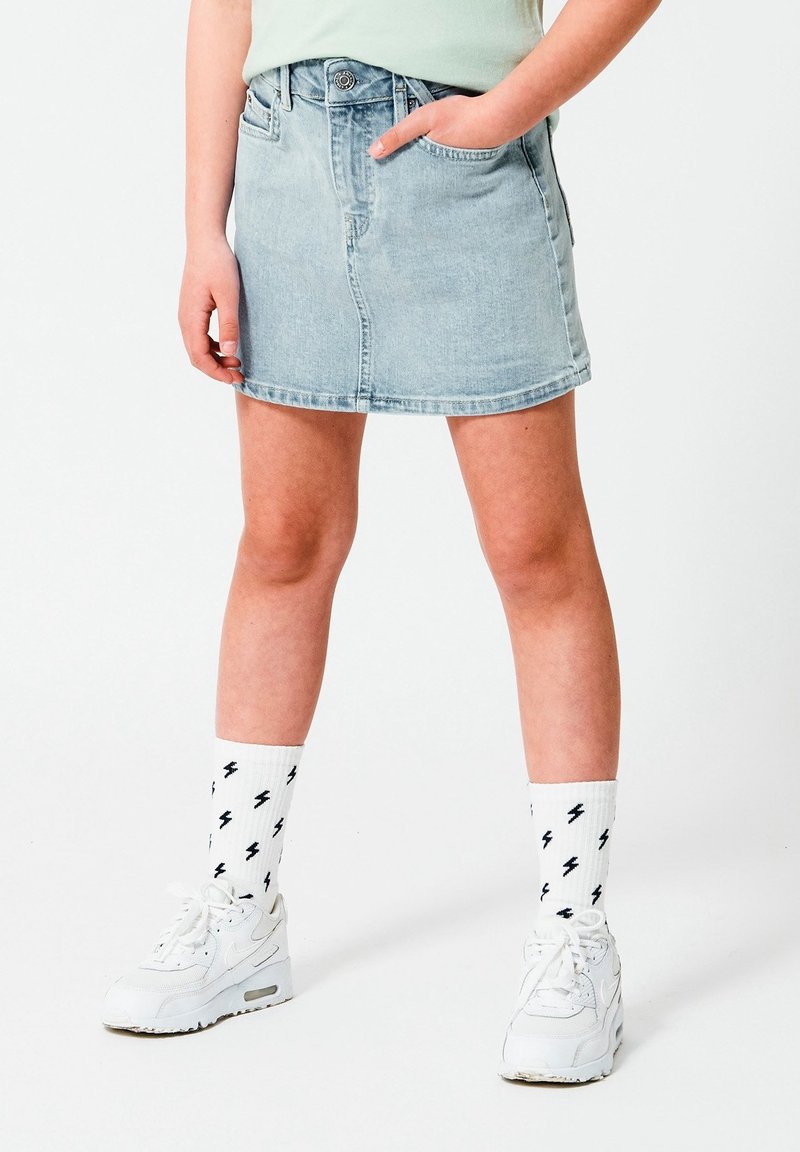 Falda mini de denim en azul claro con una cintura ajustada, cinco bolsillos y un lavado sutil. Combinada con zapatillas blancas y calcetines con rayos.