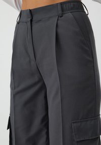 Graue Cargo-Hosen aus glattem Stoff mit Seitentaschen, lockerer Passform und elastischem Bund für zusätzlichen Komfort. Mit Falten für einen stylischen Akzent.