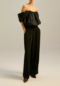 Czarny top odkrywający ramiona z marszczonym materiałem, w połączeniu z czarnymi spodniami o wysokim stanie z małymi wzorami w kształcie serc oraz czółenkami na spiczastym obcasie.