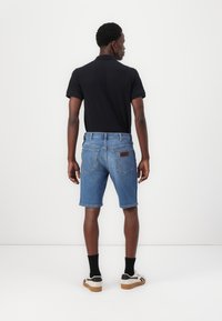 Črn polo majica, svetlo modri denim kratki hlače z zadnjimi žepi, rjav usnjen znak, bele čevlje s črnimi detajli, črne nogavice.