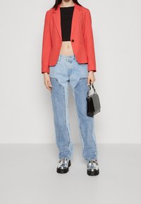 Röd kort blazer, svart topp, ljusblå baggy denimjeans med sidokanter, silvriga klumpiga skor med tjock sula och en liten svart handväska.