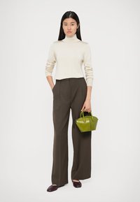 Cream turtleneck sweater, brown high-waisted trousers, small green handbag with rounded handles, and maroon shoes. Simple, clean lines.