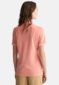 Lys pink polo shirt med korte ærmer og krave. Blød tekstur, enkelt design, med en rygventilation nederst.