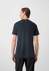 Tricou din material moale, de culoare bleumarin, cu mânecă scurtă și guler rotund, având un detaliu mic cu dungi roșii, albe și bleumarin la gulerul din spate.