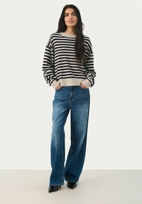 Pull en tricot rayé beige et marine, avec un col rond et une coupe oversize. Associé à un jean en denim bleu à jambes larges et des talons noirs.