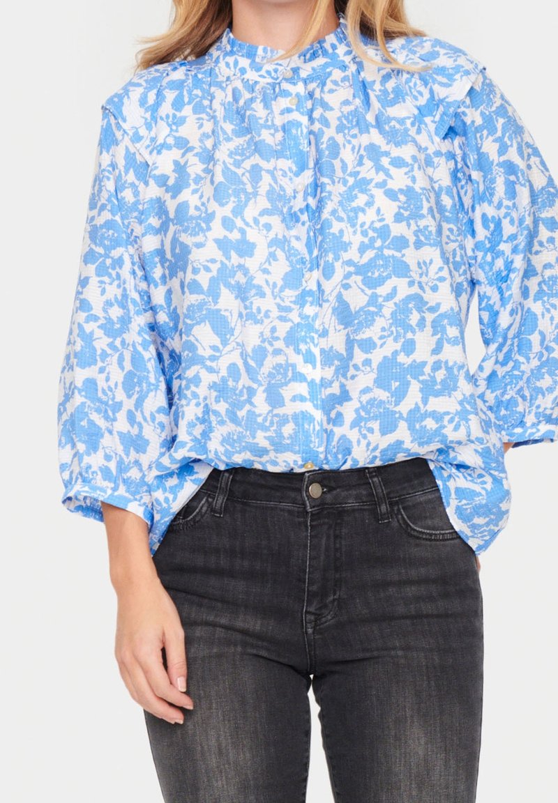 Blå blus med blommönster, hög halsringning, knappstängning och loose fit. Matchad med åtsittande svarta jeans. Texturerad tyg.