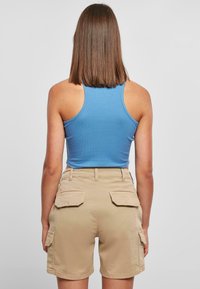 Hellblaues, geripptes Tanktop, kombiniert mit beigen Cargo-Shorts, die zwei Gesäßtaschen und zwei Seitentaschen haben, von hinten betrachtet.