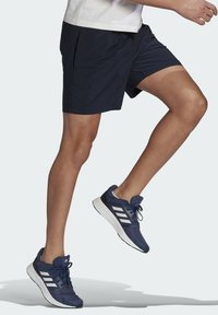 Pantalones cortos deportivos marinos con cinturilla elástica y cordón, combinados con zapatillas de running azul oscuro con rayas blancas de acento y parte superior de malla.