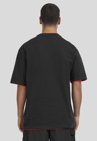 Camiseta negra de algodón con mangas cortas, que presenta un acento rojo en los bordes de las mangas y el dobladillo inferior. Vista trasera simple.