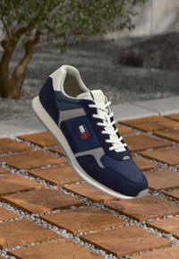 Marineblauwe hardloopschoen met witte accenten, een mesh zijpaneel en een gestructureerde rubberen zool. Heeft contrasterende logo-details en veters.