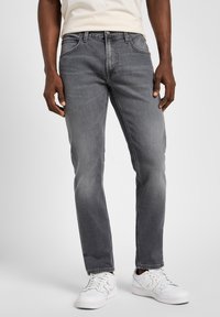 Grey denim jeans with a straight fit, subtle fading, five-pocket design, and metal hardware accent. Paired with white athletic sneakers.