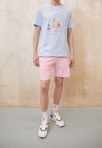T-shirt en coton bleu clair avec un design graphique, associé à un short rose. Les chaussures présentent des accents multicolores et des semelles rembourrées.