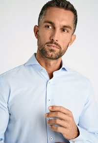 Lichtblauw geruite overhemden met een spread collar, voorzien van witte knopen en een gladde textuur. Handen in een neutrale positie bij de borst.