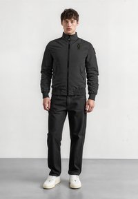 Mustat bombersati takki, jossa on korkea kaulus, vetoketjukiinnitys ja sivutaskut. Yhdistetty mustiin housuihin ja valkoisiin tennareihin. Silkkinen kangas ja räätälöity istuvuus.