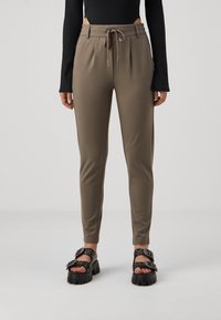 Pantaloni aderenti verde oliva con vita a cordino, tasche laterali, gambe affusolate e texture liscia. Abbinati a sandali neri spessi.