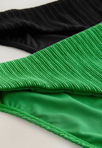 Tissu de maillot de bain noir et vert avec des surfaces texturées et côtelées ; le vert a une doublure intérieure lisse. Les sections se chevauchent légèrement.