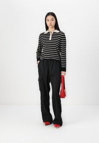 Polo a maniche lunghe a righe bianche e nere con colletto beige, abbinato a pantaloni cargo neri e tacchi a punta rossi con borsa abbinata.