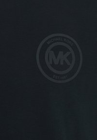 Camiseta azul escura feita de algodão, com um logótipo redondo com "MICHAEL KORS" e "EST. 1981" em impressão escura ao centro.