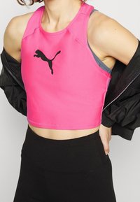 Top corto senza maniche rosa realizzato in tessuto elasticizzato, con un logo di gatto nero sul davanti, abbinato a leggings neri a vita alta.
