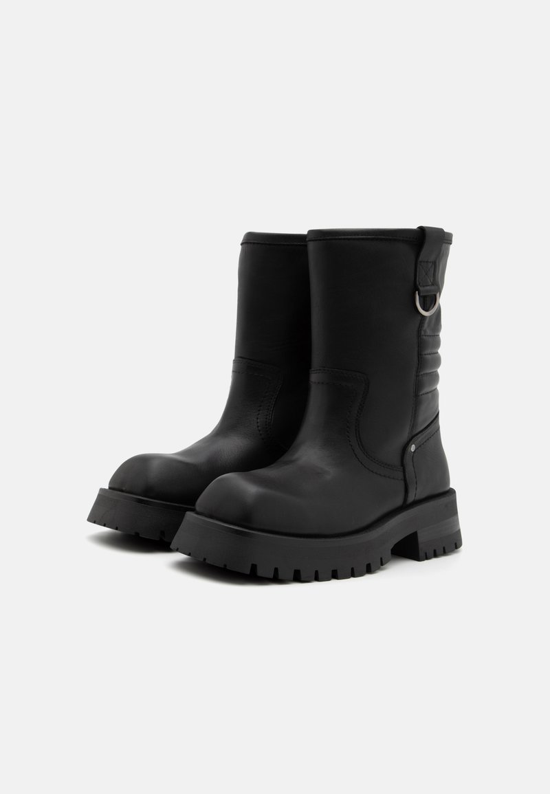 Stivaletti in pelle nera con suola spessa e rigata. Presentano un anello laterale e dettagli cuciti lungo le sezioni superiori. Finitura liscia.