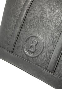 Szara skórzana torebka o teksturowanej powierzchni, z pionowymi szwami i okrągłym wytłoczonym logo z napisem 'B.'.