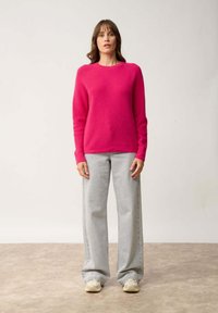 Helderroze gebreide trui, ronde hals, lange mouwen, gecombineerd met lichtgrijze wijde jeans. Eenvoudige schoenen maken de outfit compleet.