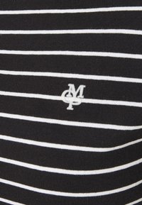 Mustat ja valkoiset raidalliset T-paita, joka on valmistettu pehmeästä kankaasta. Vasemmalla puolella on pieni valkoinen brodeerattu logo.