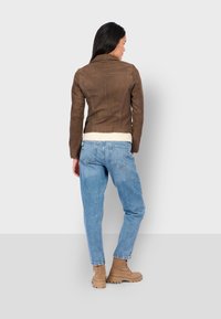 Hnědá nubuková bunda s přiléhavým střihem, s vysokým límcem a krémovou umělou kožešinou. Spárováno se světle modrými džíny a bezovými botami.