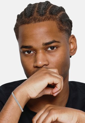 Modèle avec des cheveux tressés, portant un t-shirt noir. Les caractéristiques notables incluent une peau lisse et un bracelet gris au poignet, avec les mains placées de manière réfléchie.