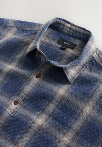 Tengerészkék kockás ing világosbarna és krémszínű díszítésekkel. Gombos gallér, mellzseb, texturált anyag és barna gombok. Látható márkacímke.