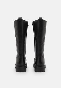 Botas de cuero negro hasta la rodilla con un acabado suave, que cuentan con cremalleras laterales y un tacón grueso. La vista trasera destaca las líneas limpias y el diseño minimalista.