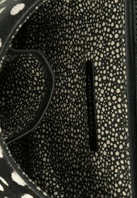 Black and cream interior of a bag with a dotted pattern. Includes a black label with text. Textured fabric with smooth edges.