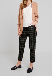 Jasnoróżowy żakiet, biały top, czarne spodnie w kratę i czarne mokasyny. Żakiet ma złote guziki; spodnie są zwężane i mają wzór w kratę.