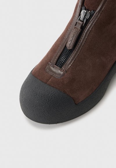 Brune ruskinds ankelstøvle med en sort tekstureret gummitoe cap og lynlåslukning i siden for nem på- og aftagning. Glat finish med subtile detaljer.