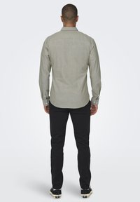 Hellgraues Langarmshirt mit button-down Kragen, strukturiertem Stoff, Rückenteilnahtdetails und schwarzen Slim-Fit-Hosen.