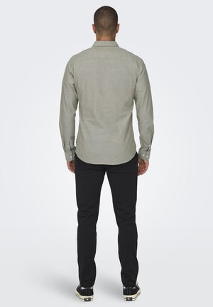 Camisa de manga larga gris claro con cuello de botón, tejido texturizado, detalles en la costura de la yugo trasero y pantalones negros de corte ajustado.
