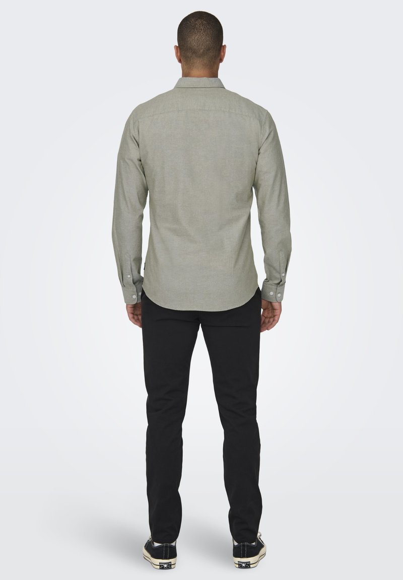 Hellgraues Langarmshirt mit button-down Kragen, strukturiertem Stoff, Rückenteilnahtdetails und schwarzen Slim-Fit-Hosen.