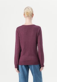 Burgundy stickad tröja med långa ärmar och ribbad nederkant, visad bakifrån. Matchad med löst sittande blå denimbyxor.