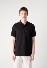 Sort polo skjorte med klassisk design, kortærmede, krave og et lille logo-patch på venstre side. Fremstillet af bomuldsmateriale.