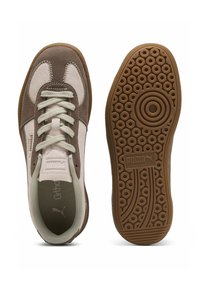 Zapatillas marrones y beige con materiales de gamuza y malla, cordones redondos, suela de goma con patrones circulares y interior acolchado.